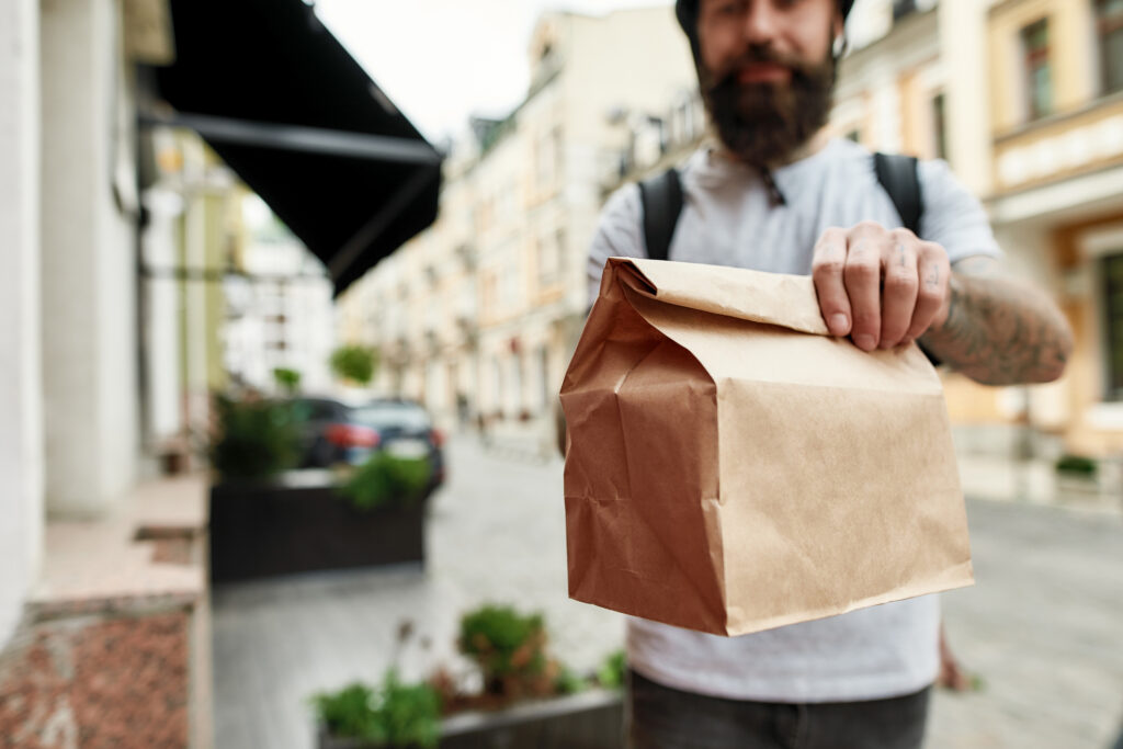 Delivery man holding paper bag while giving away order to a customer. 