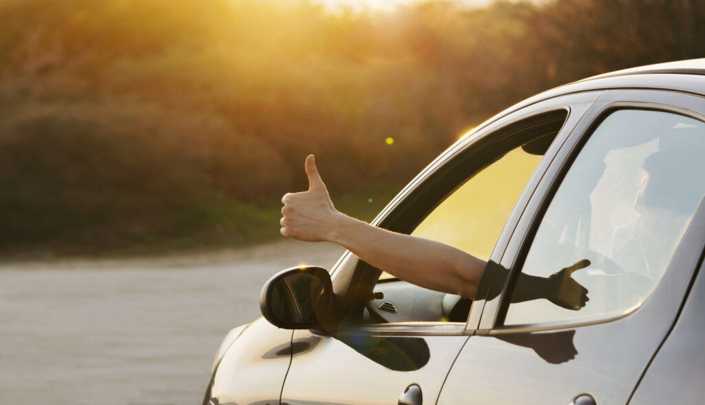Man showing thumbs up from car window.