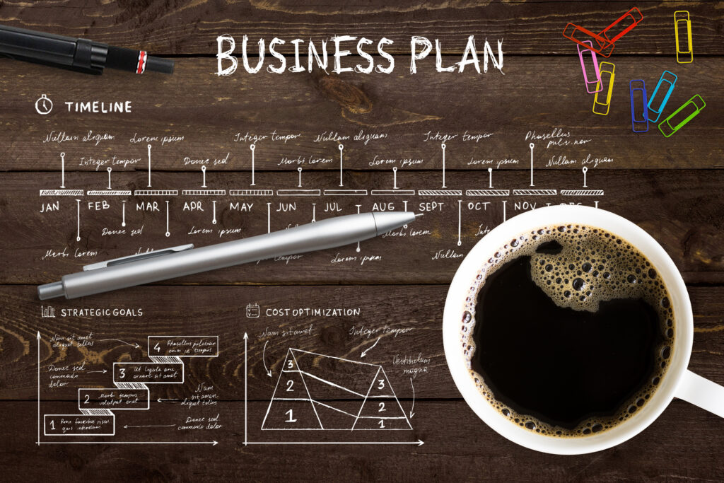 Close-up view from above of a professional desk with a cup full of hot coffee, colored paper clips and a pen on a complex written business plance