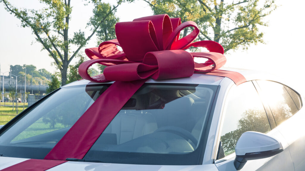 New car gift. New car with red gift ribbon and bow awaits its buyer in the cabin. Auto dealership and rental concept background.