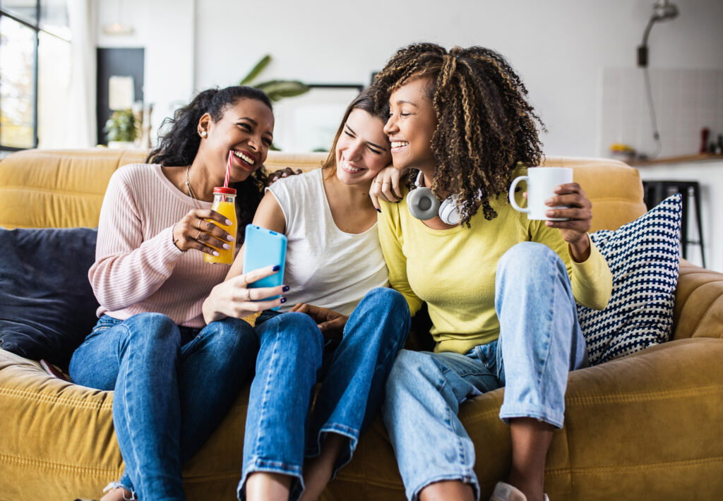 Cheerful female friends enjoying free time together at home - Three happy young adult women hanging out while - Friendship and social gathering concept