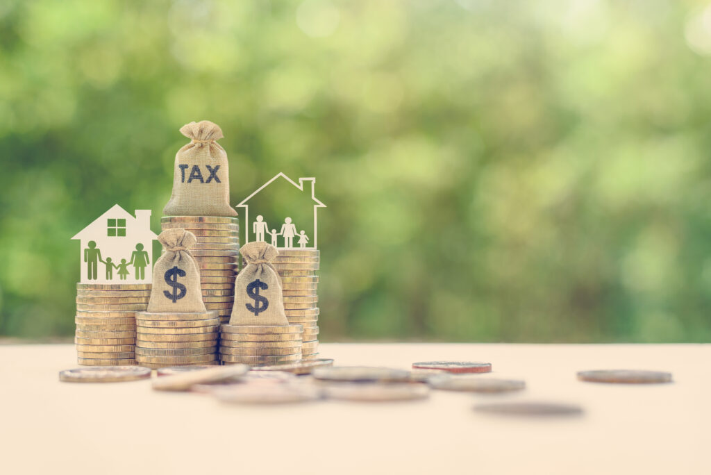 Family tax benefit/residential property or estate tax concept: Tax burlap bag, family members, house on rows of coin or money. Taxes can impact investing in a variety of ways.