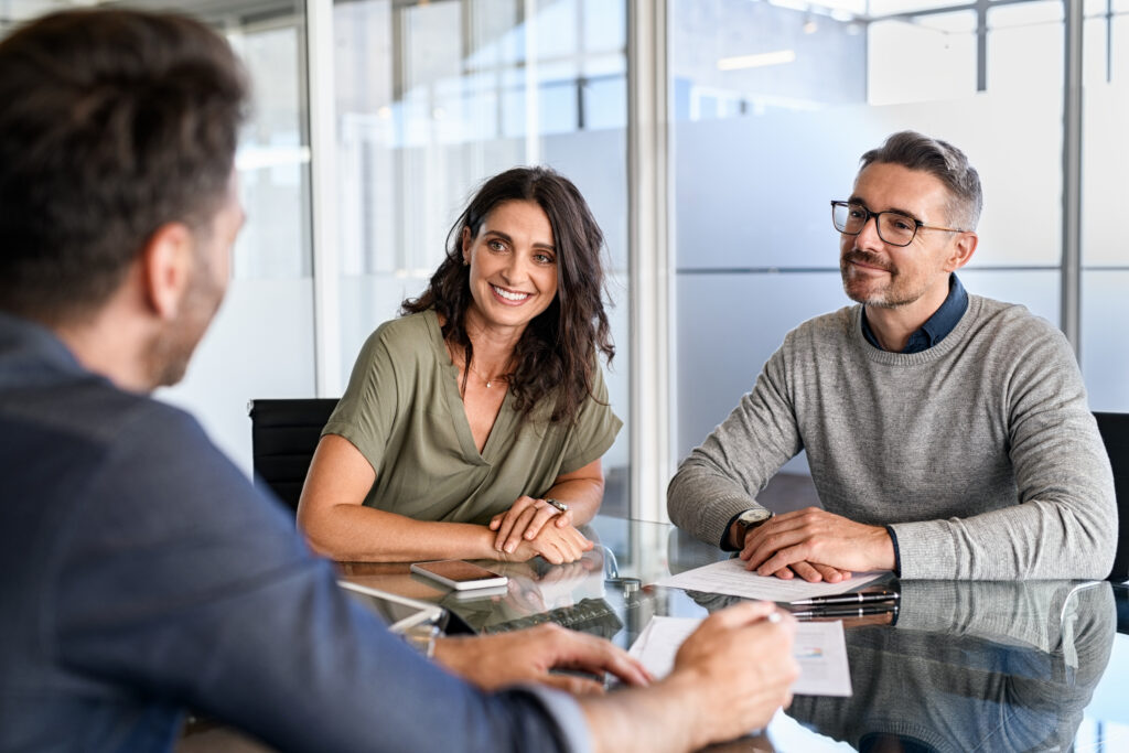 Smiling mature couple meeting with bank manager for investment. mid adult woman with husband listening to businessman during meeting in conference room in modern office. Happy middle aged couple meeting financial advisor.