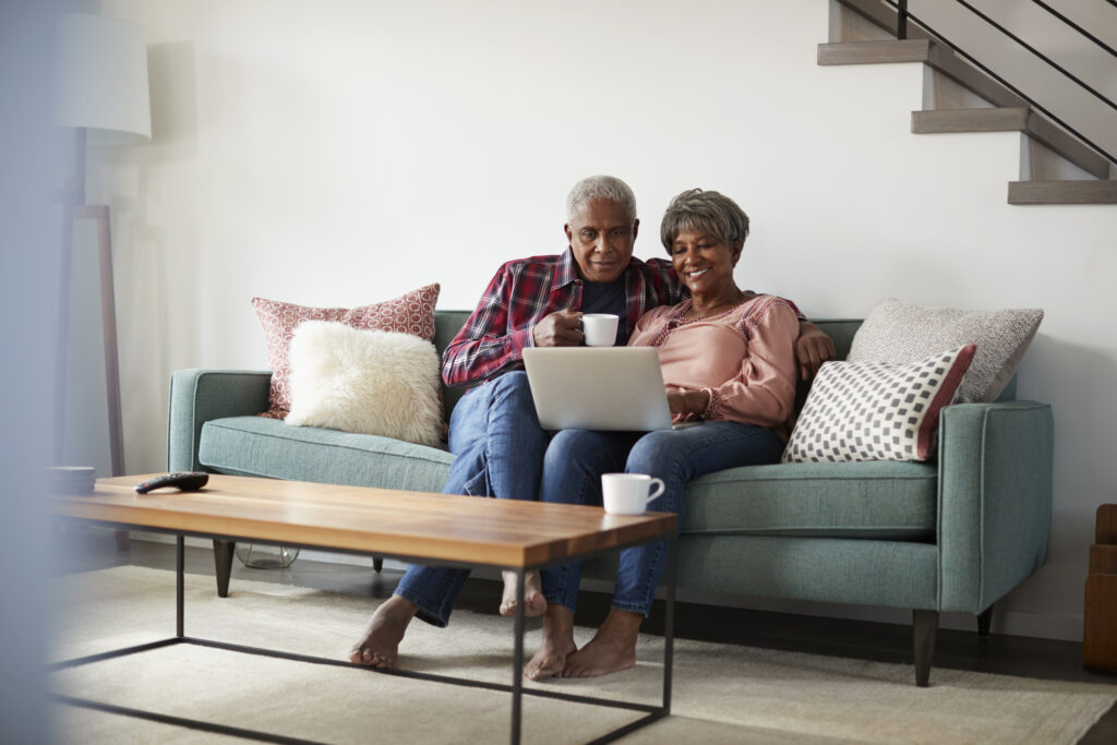 Senior Couple Sitting On Sofa At Home Using Laptop To Buy Insurance Online