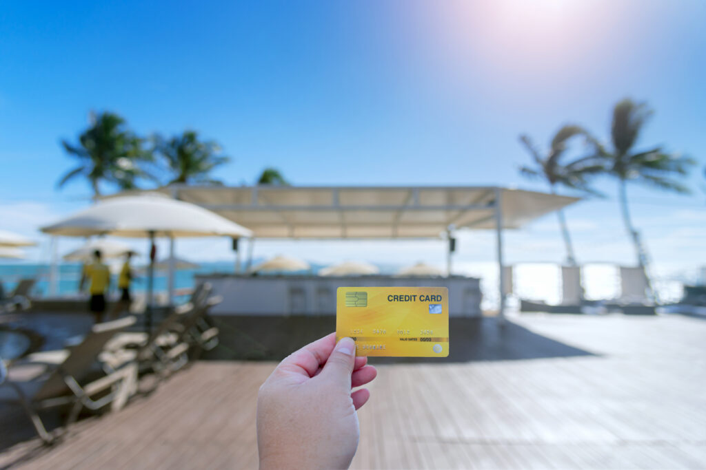 Hand holding credit card used for travel. Travel expenses credit card on holiday on blurred resort background. 