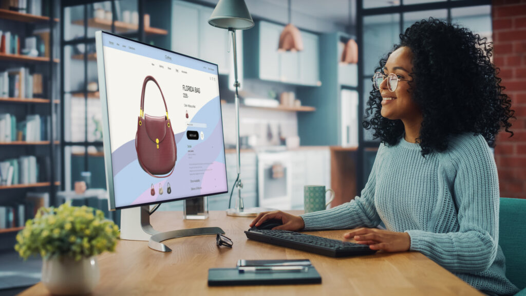 Female Using Desktop Computer with Clothing Online Web Store to Choose and Buy Clothes from New Collection. Female Browsing the Internet at Home Living Room while Sitting at a Table