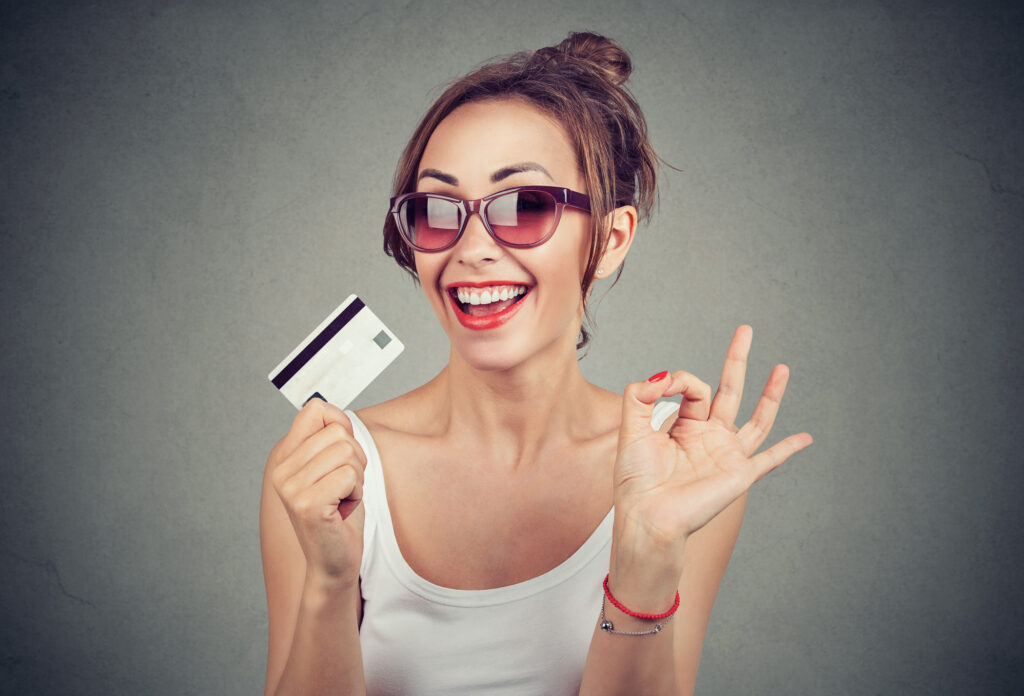 happy young woman in sunglasses with credit card giving ok hand sign gesture