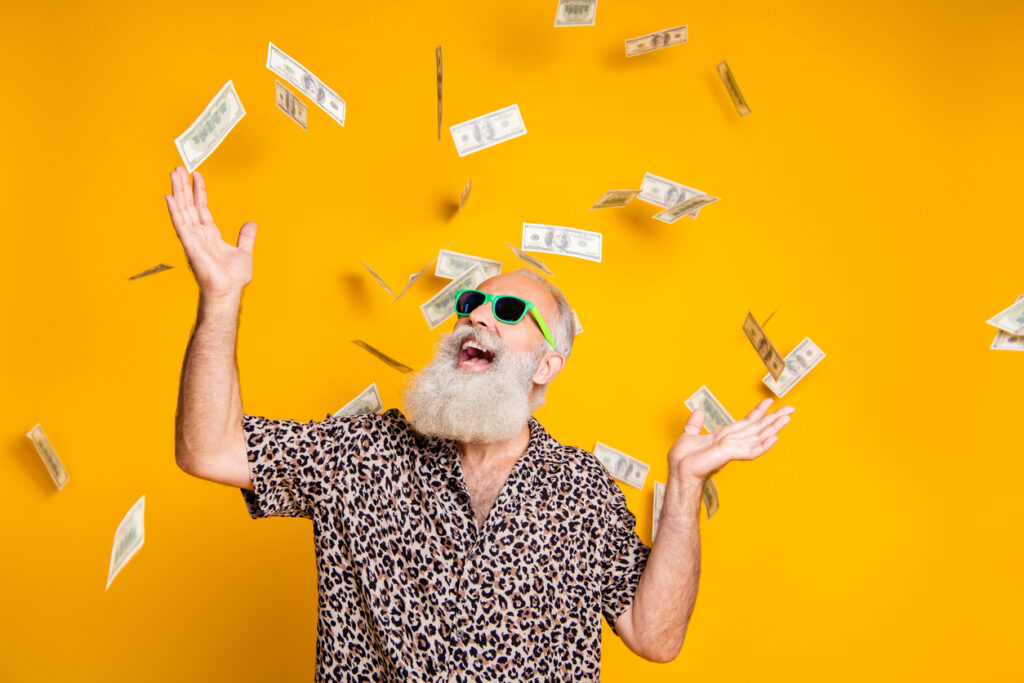 Portrait of crazy funky funny old bearded man hipster in green eyeglasses, eyewear look up at money falling, leopard stylish shirt isolated over yellow background