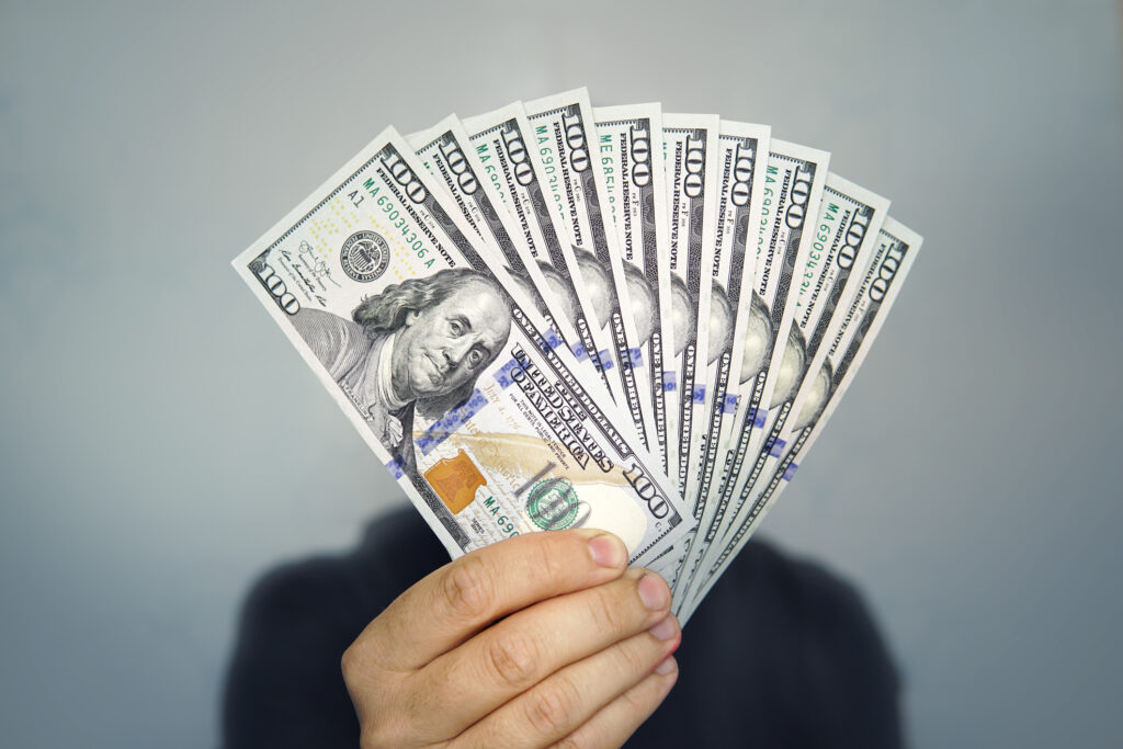 Hands holding dollar cash. 1000 dollars in 100 bills in a man's hand close-up on a dark background.