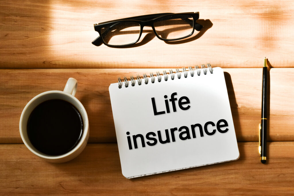 LIFE INSURANCE text written in a notepad near a cup coffee, eyeglasses and pen on a wooden background. Business concept.