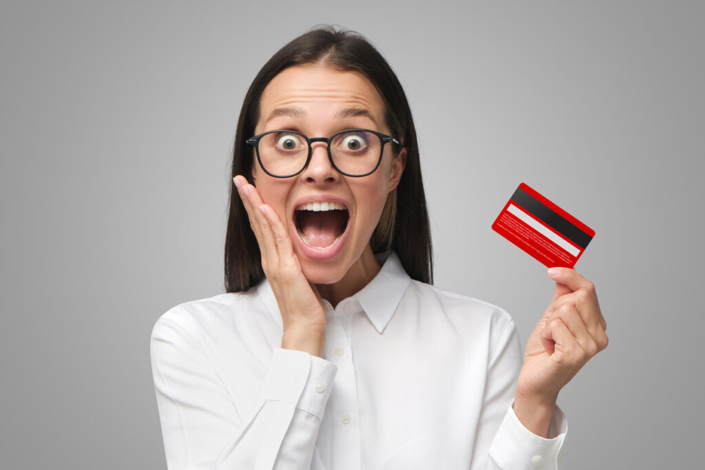 Excited young woman with mouth open, holding credit card, isolated on gray background