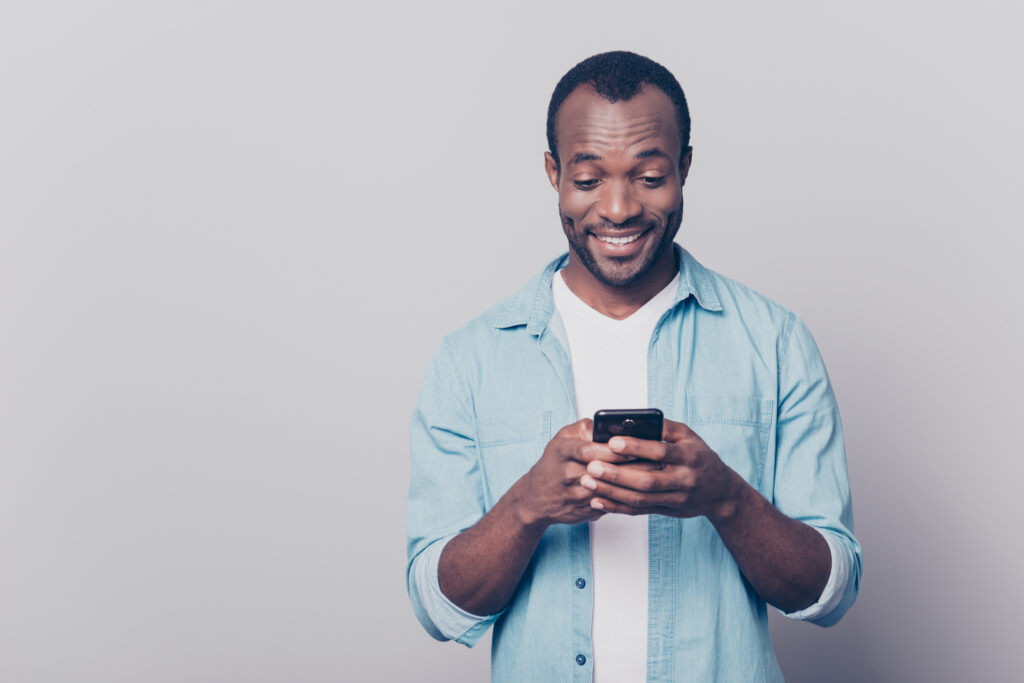 Portrait of handsome excited cheerful joyful delightful curious guy wearing casual jeans denim shirt using apps on his mobile phone 