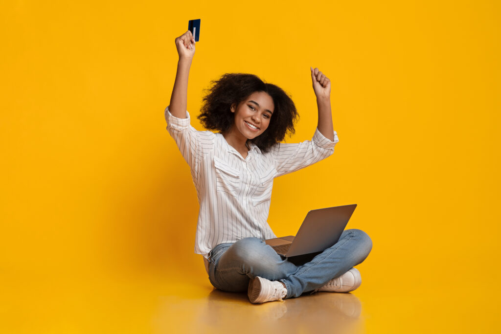 Portrait Of Happy Woman Celebrating Success With Laptop And Credit Card, Raising Hands In Excitement, Yellow Background