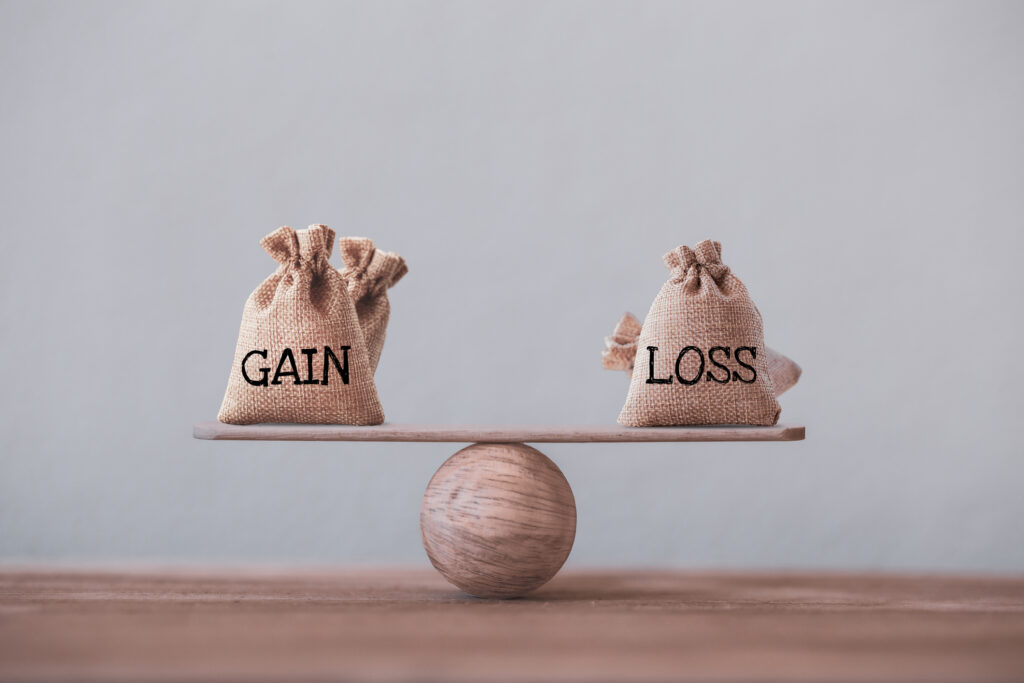 Gain and loss bags on a basic balance scale on a blackboard. Capital investment gain and loss, financial concept, depicts balancing between profit and loss while managing assets
