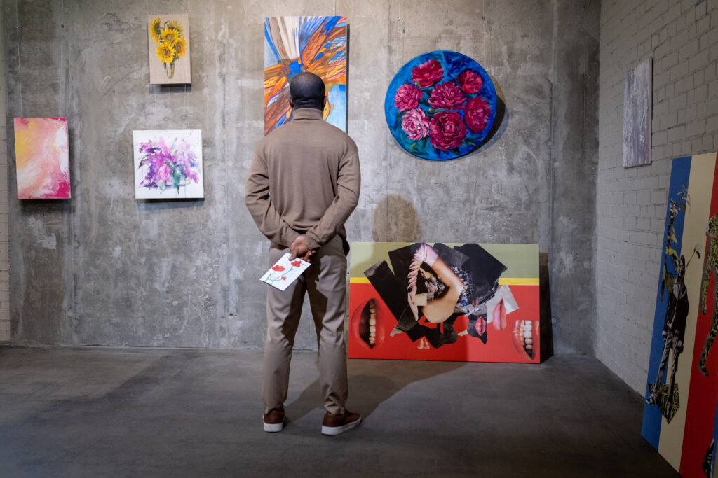 Rear view of man standing in front of the wall with paintings and looking at them in art gallery